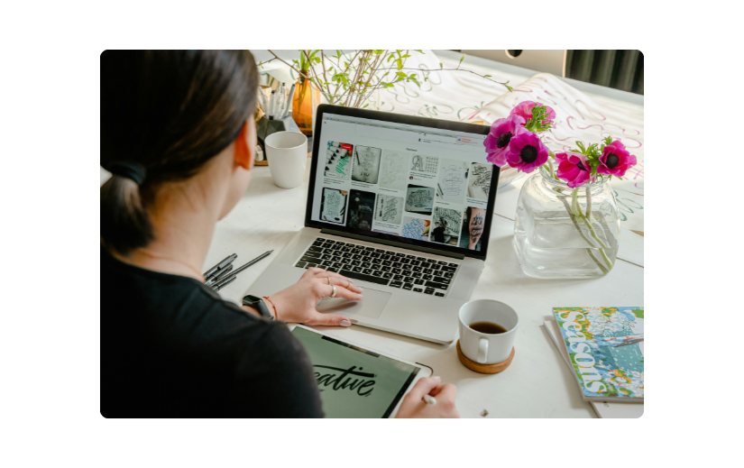 Person designing an online store on a laptop with a dropshipping website builder, surrounded by materials and flowers.